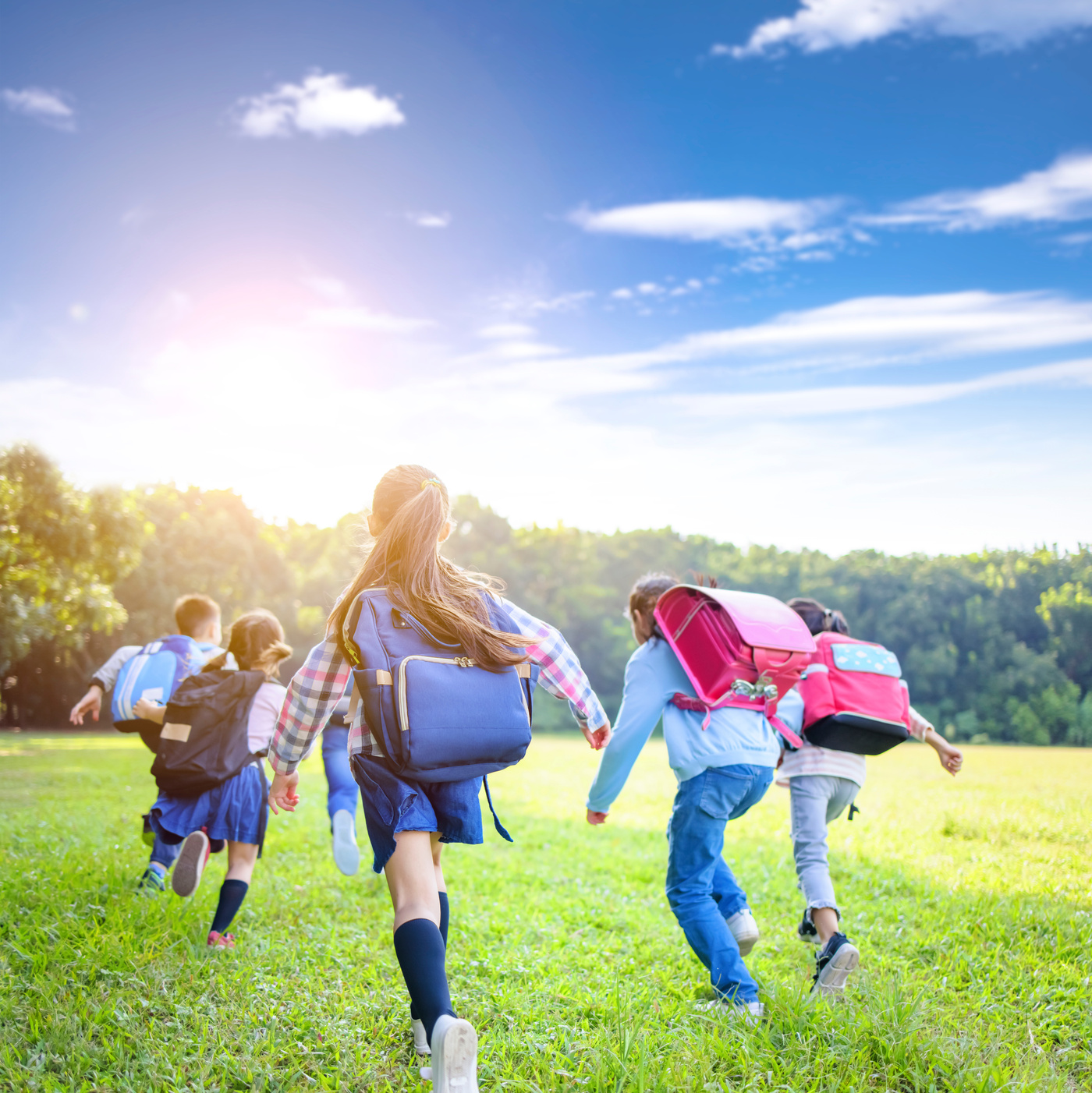 rear view of elementary school kids running on the grass